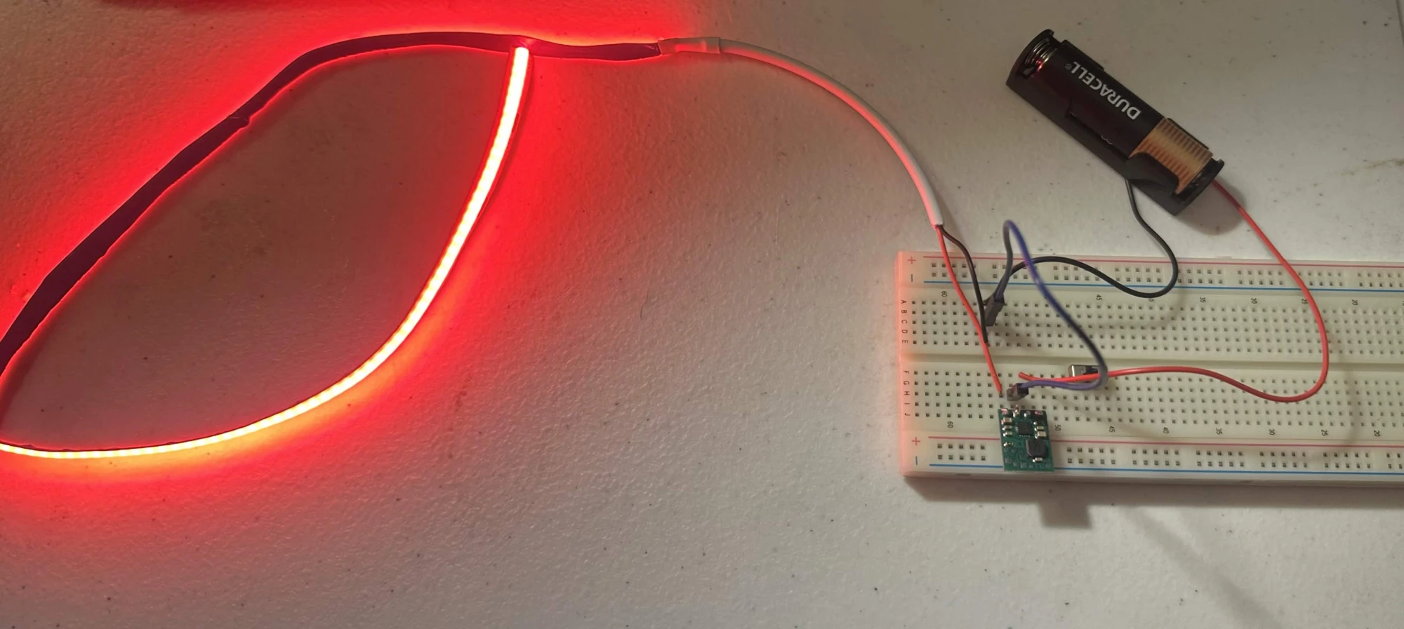Breadboard circuit with an AA battery holder and Pololu step-up regulator lighting a red COB LED strip
